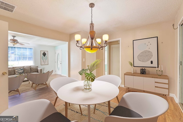 dining room with a textured ceiling, baseboards, visible vents, light wood-style floors, and ceiling fan with notable chandelier