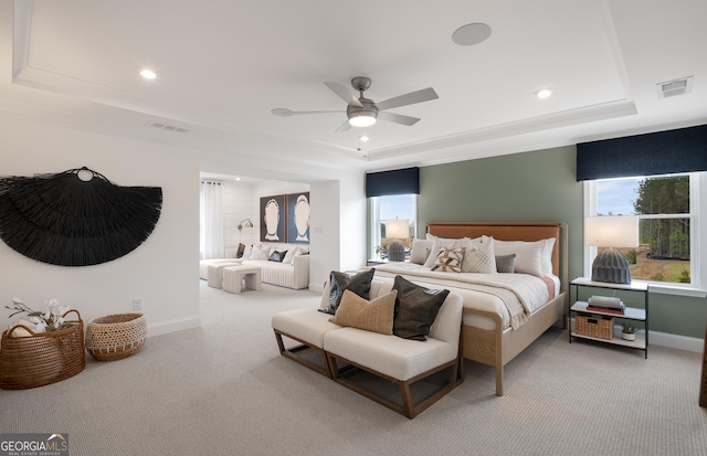 bedroom with multiple windows, ceiling fan, a tray ceiling, and light colored carpet