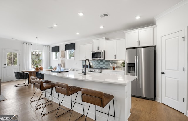 kitchen with white cabinets, a center island with sink, appliances with stainless steel finishes, and a breakfast bar