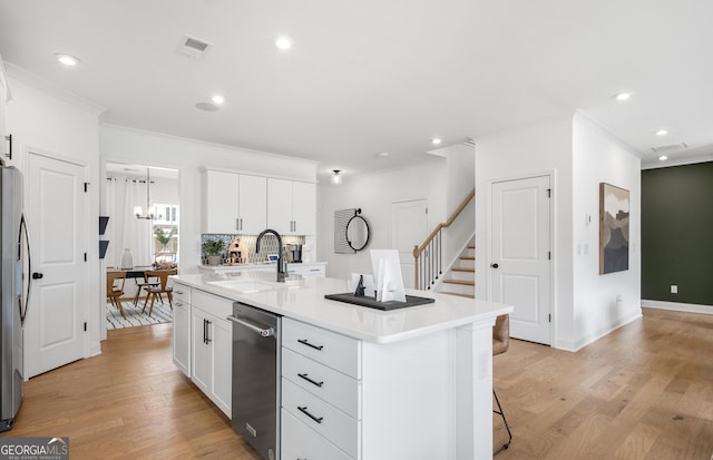 kitchen with stainless steel appliances, sink, white cabinetry, light hardwood / wood-style flooring, and a center island with sink