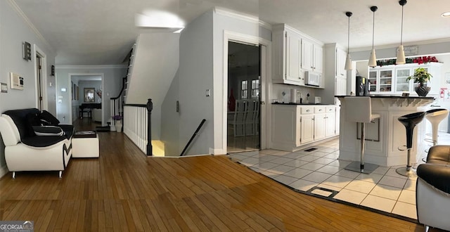 kitchen featuring hanging light fixtures, ornamental molding, a breakfast bar, refrigerator, and white cabinetry