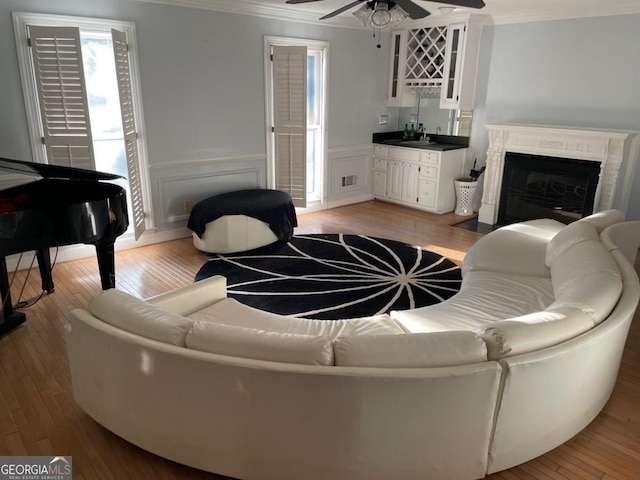 living room with light wood-type flooring, ceiling fan, ornamental molding, and indoor wet bar