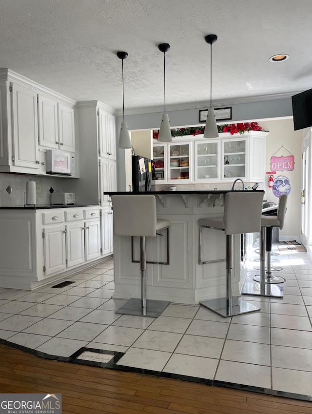 kitchen featuring crown molding, a breakfast bar, black fridge, pendant lighting, and white cabinetry