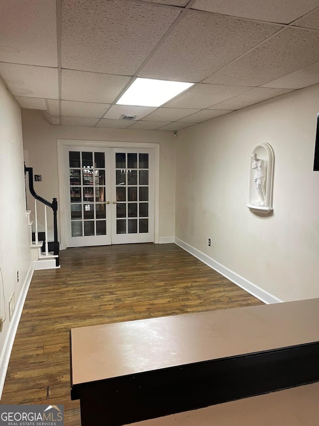 exercise room featuring dark wood-type flooring, french doors, and a paneled ceiling