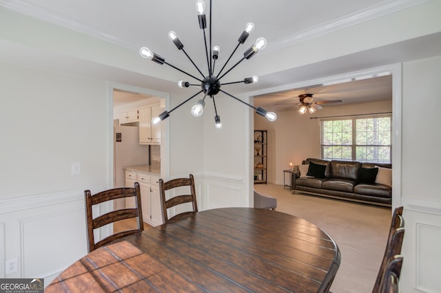 carpeted dining room featuring ceiling fan, ornamental molding, wainscoting, and a decorative wall