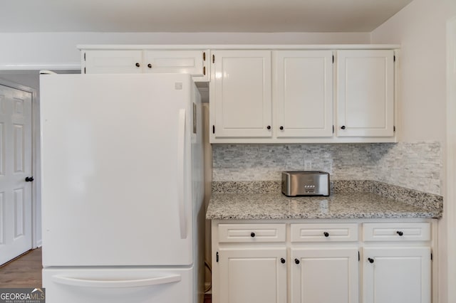 kitchen featuring wood finished floors, decorative backsplash, freestanding refrigerator, and white cabinetry