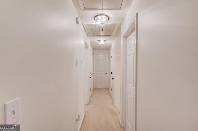 corridor featuring baseboards, attic access, and light colored carpet