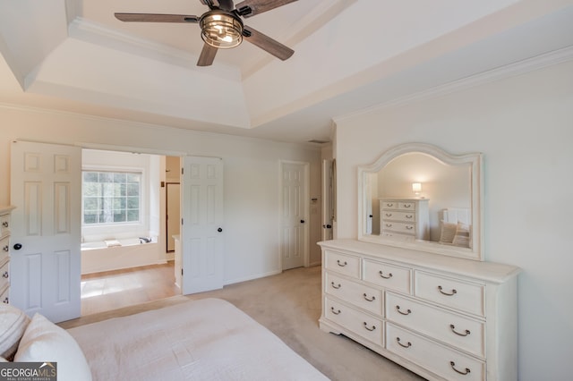 bedroom featuring a tray ceiling, crown molding, light colored carpet, ensuite bathroom, and a ceiling fan