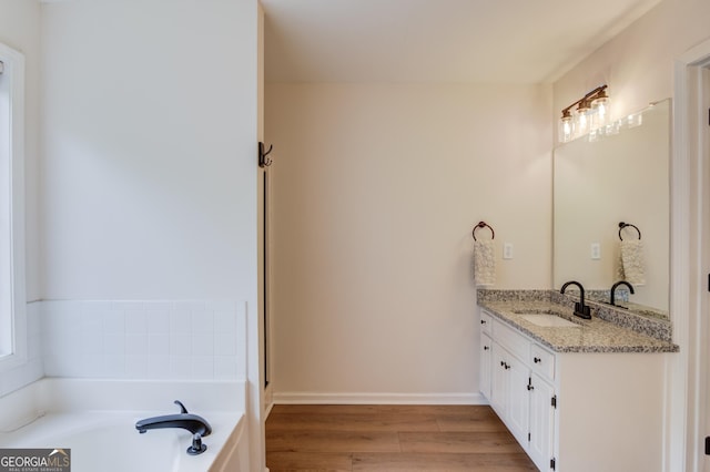 bathroom featuring baseboards, vanity, a bath, and wood finished floors