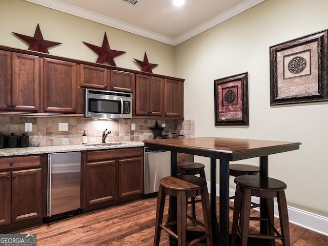 kitchen with sink, hardwood / wood-style floors, stainless steel appliances, tasteful backsplash, and ornamental molding