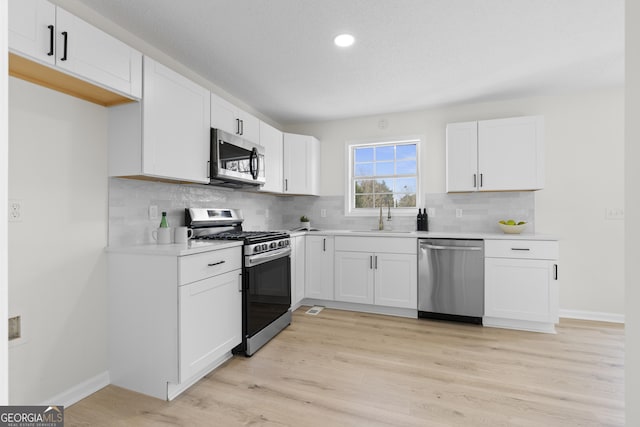 kitchen featuring stainless steel appliances, white cabinetry, sink, and light hardwood / wood-style flooring