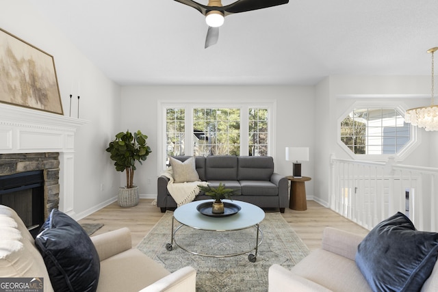 living room with ceiling fan with notable chandelier, light hardwood / wood-style flooring, and a stone fireplace