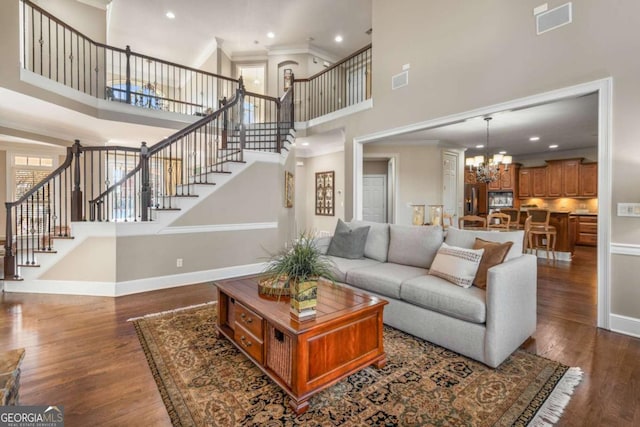 living room with a high ceiling, dark wood-type flooring, crown molding, and a chandelier