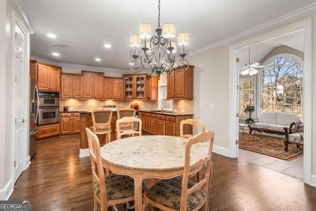 dining room with sink, dark wood-type flooring, crown molding, and ceiling fan with notable chandelier