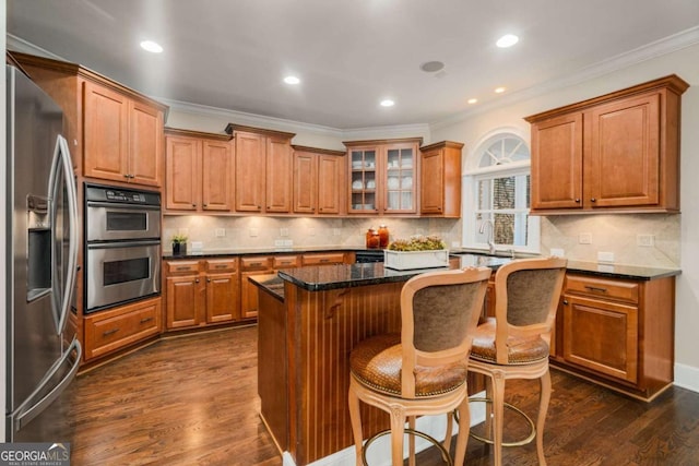 kitchen featuring stainless steel appliances, dark stone counters, dark hardwood / wood-style floors, a kitchen island, and a breakfast bar