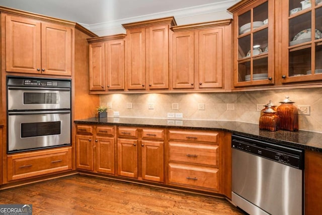 kitchen with stainless steel appliances, ornamental molding, backsplash, dark stone counters, and dark hardwood / wood-style flooring