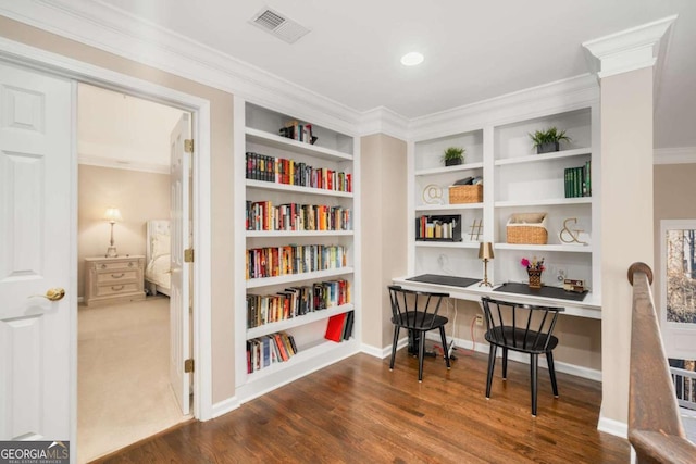 interior space with built in shelves, built in desk, crown molding, and hardwood / wood-style floors