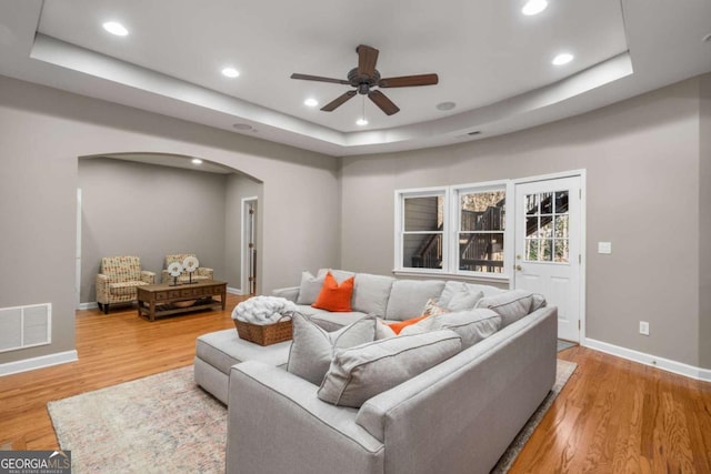 living room with ceiling fan, hardwood / wood-style floors, and a tray ceiling