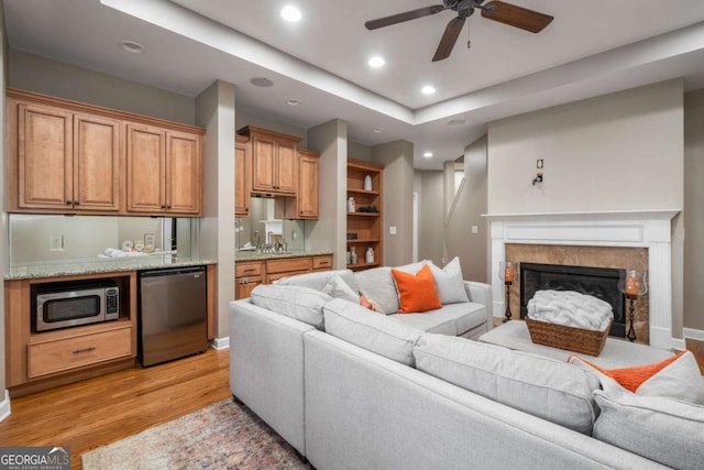 living room featuring sink, a fireplace, ceiling fan, and light hardwood / wood-style floors