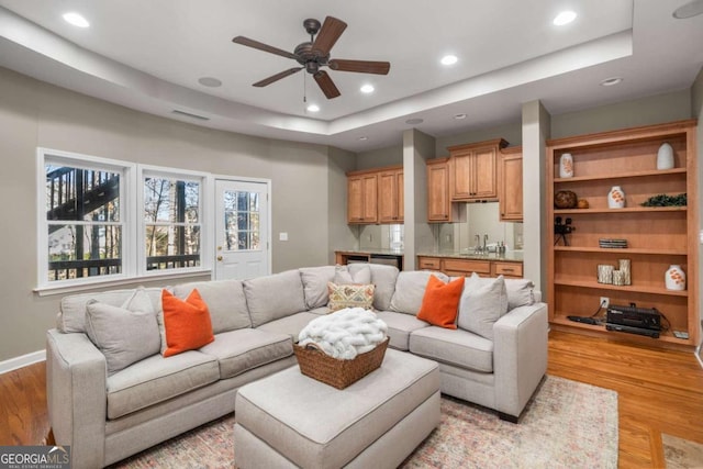 living room with sink, ceiling fan, a tray ceiling, and light hardwood / wood-style flooring