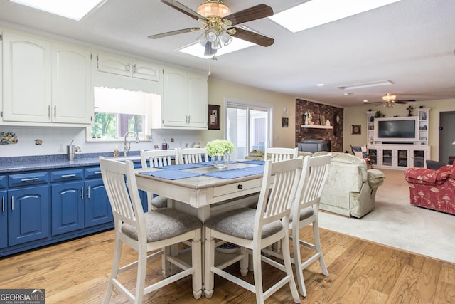 dining room with a fireplace, ceiling fan, a skylight, and light hardwood / wood-style flooring