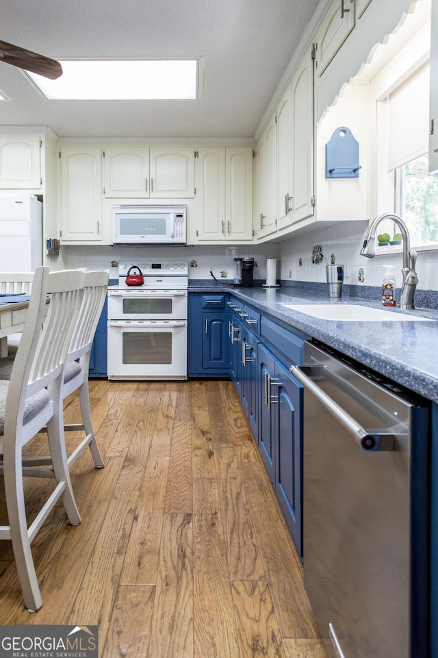 kitchen featuring white appliances, blue cabinetry, light wood-type flooring, sink, and white cabinetry