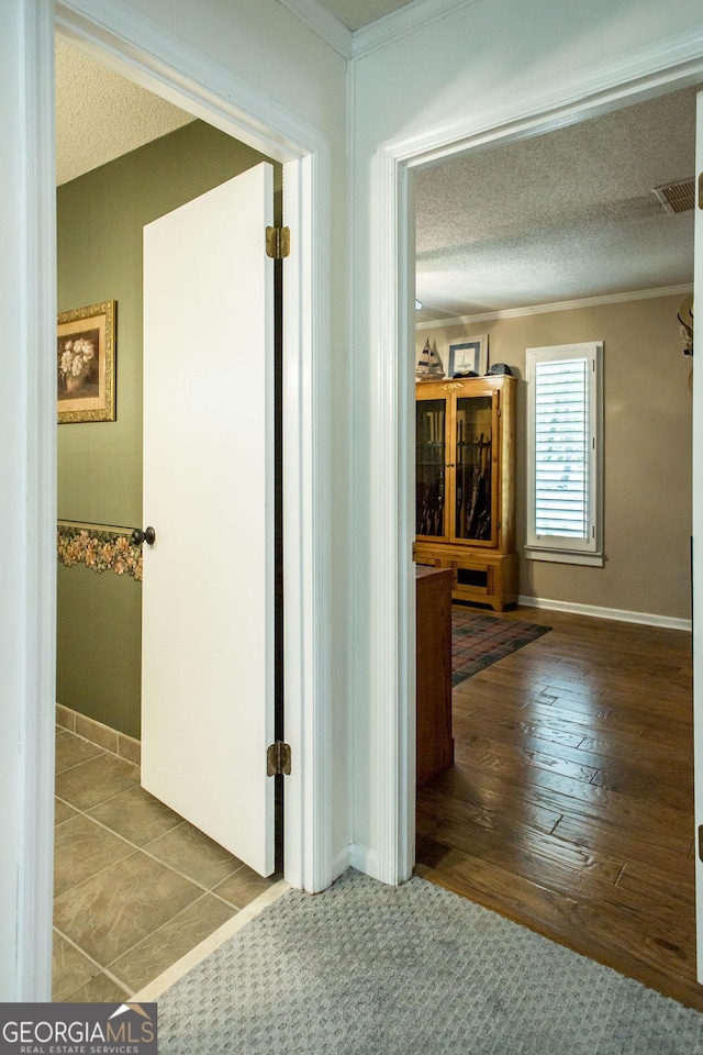 hall with tile patterned flooring, a textured ceiling, and crown molding