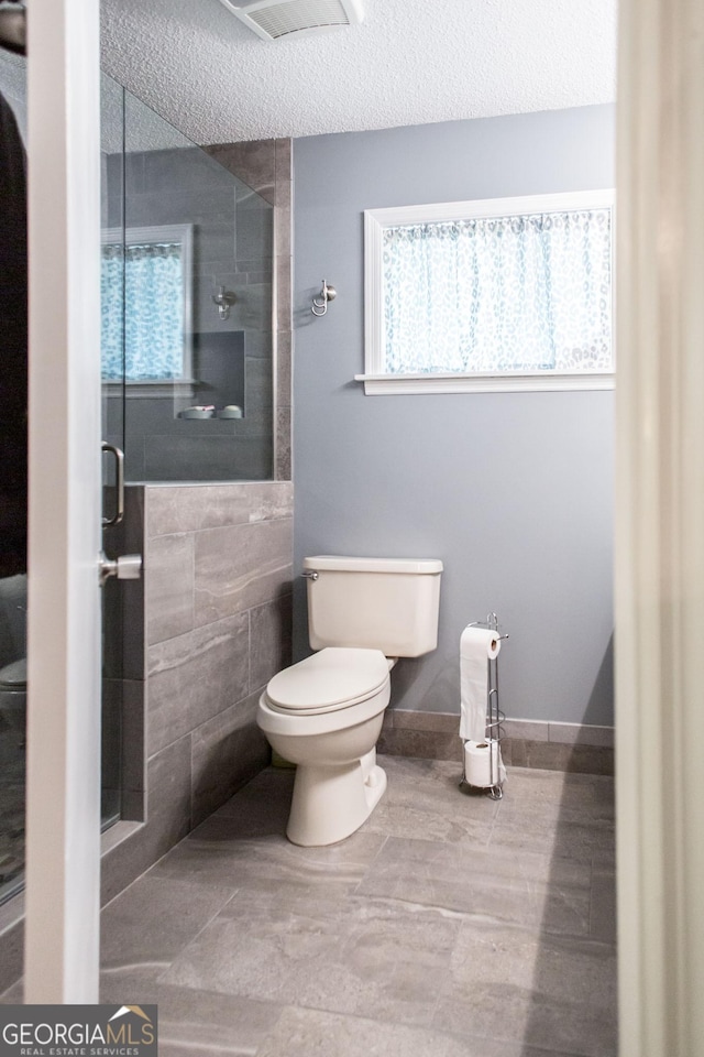 bathroom with toilet, a textured ceiling, a shower with shower door, and a wealth of natural light