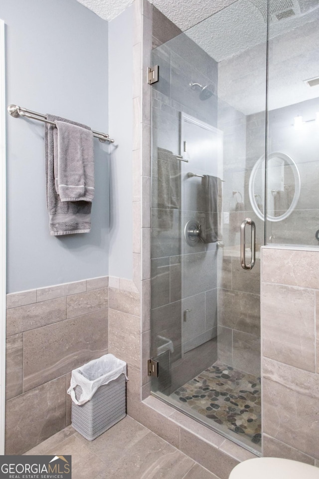 bathroom featuring tile walls, tile patterned flooring, walk in shower, and a textured ceiling