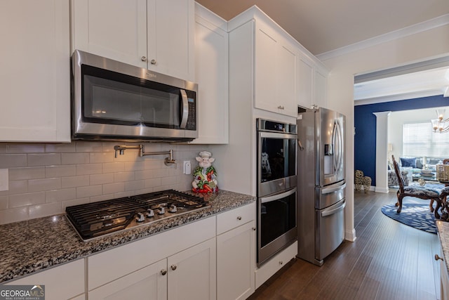 kitchen with appliances with stainless steel finishes, dark stone counters, dark hardwood / wood-style flooring, decorative backsplash, and white cabinets