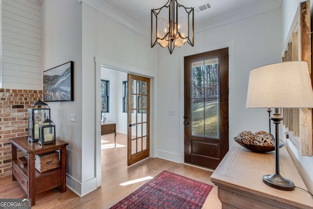 foyer entrance featuring ornamental molding, light wood-type flooring, a notable chandelier, and french doors