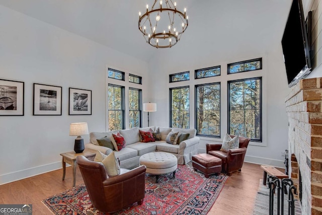 living room with hardwood / wood-style floors, high vaulted ceiling, a brick fireplace, and a chandelier