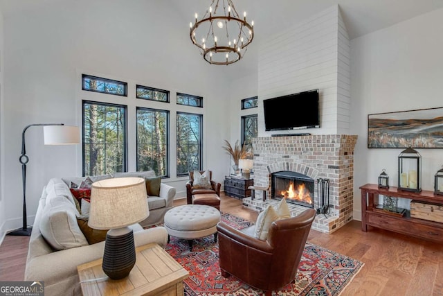 living room featuring a high ceiling, a brick fireplace, light wood-type flooring, and an inviting chandelier