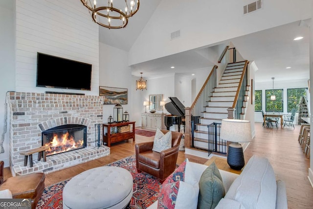 living room featuring a brick fireplace, high vaulted ceiling, light hardwood / wood-style floors, and an inviting chandelier