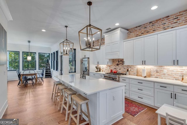 kitchen with white cabinets, hanging light fixtures, brick wall, a center island with sink, and appliances with stainless steel finishes