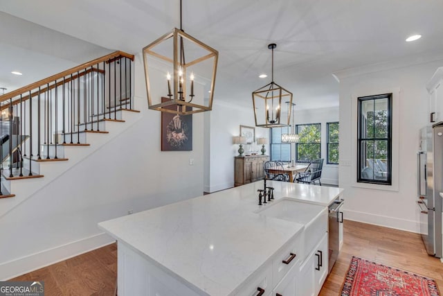 kitchen with a kitchen island with sink, light hardwood / wood-style flooring, hanging light fixtures, and white cabinetry