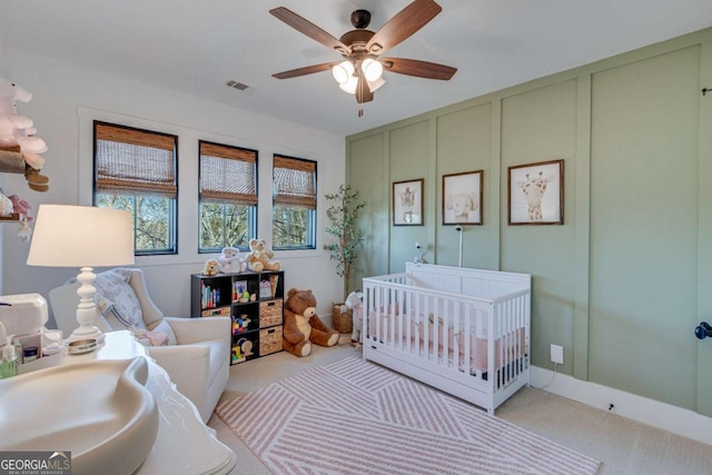 carpeted bedroom with ceiling fan and a nursery area