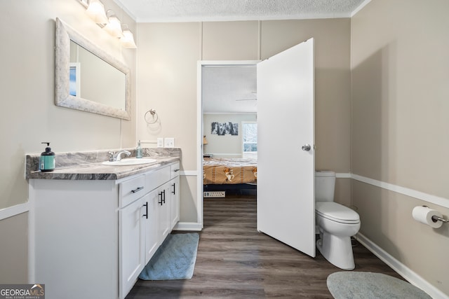 bathroom with toilet, a textured ceiling, ornamental molding, wood-type flooring, and vanity