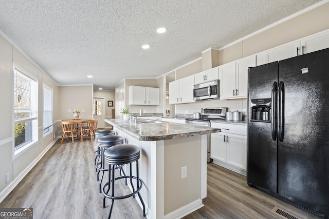 kitchen with stainless steel appliances, white cabinets, crown molding, and an island with sink