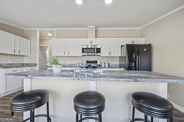 kitchen with stainless steel appliances, white cabinets, a textured ceiling, and a kitchen island with sink