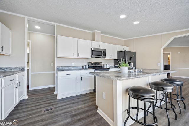 kitchen featuring white cabinets, a textured ceiling, an island with sink, and appliances with stainless steel finishes