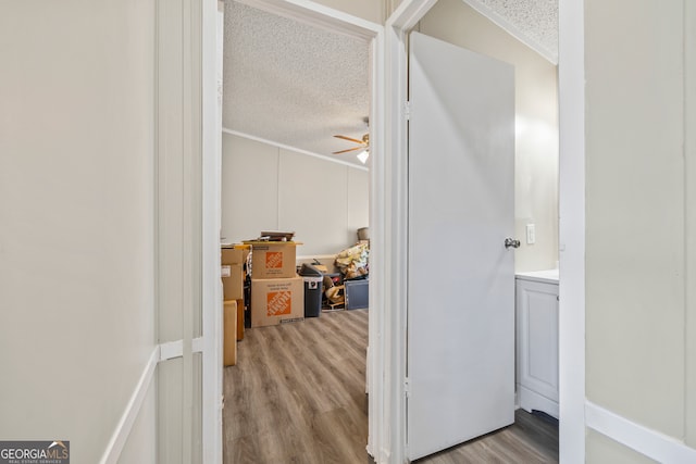 hallway featuring a textured ceiling, light wood-type flooring, and crown molding