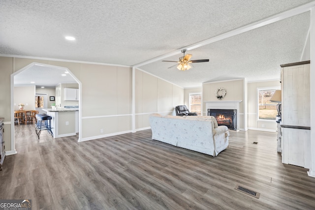 living room with a textured ceiling, dark hardwood / wood-style flooring, crown molding, and ceiling fan