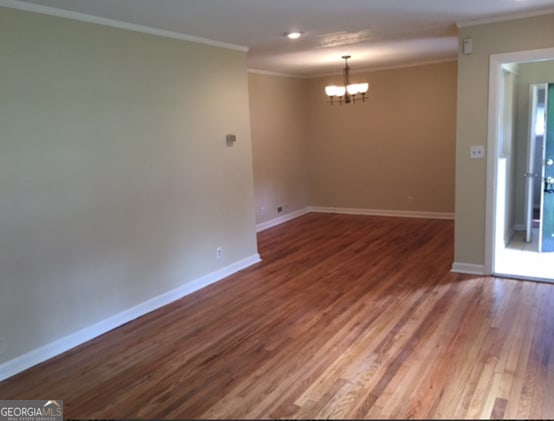 unfurnished room with an inviting chandelier, hardwood / wood-style flooring, and crown molding