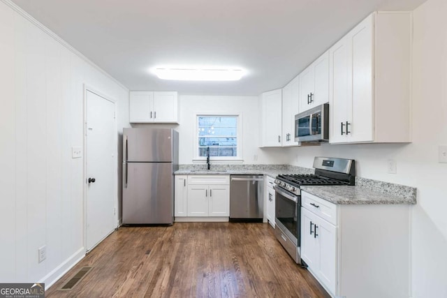 kitchen with light stone counters, dark wood-type flooring, stainless steel appliances, white cabinets, and sink