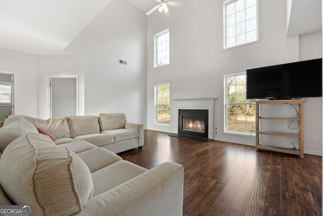 living room with a high ceiling, ceiling fan, a healthy amount of sunlight, and dark hardwood / wood-style floors