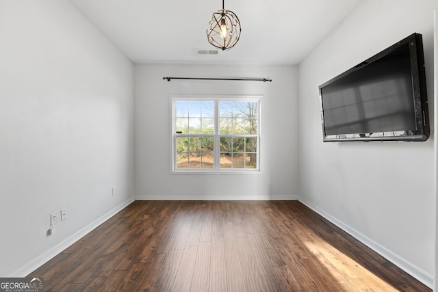 spare room with a notable chandelier and dark wood-type flooring