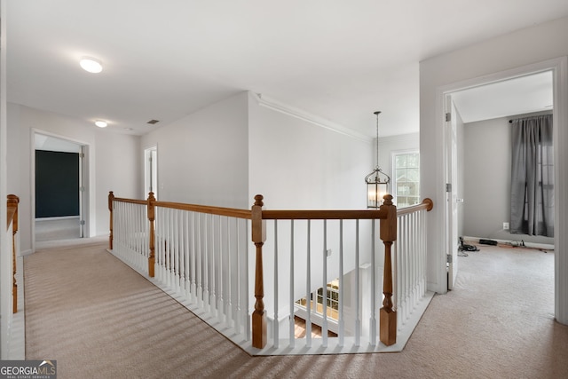 hall with an inviting chandelier, crown molding, and light colored carpet