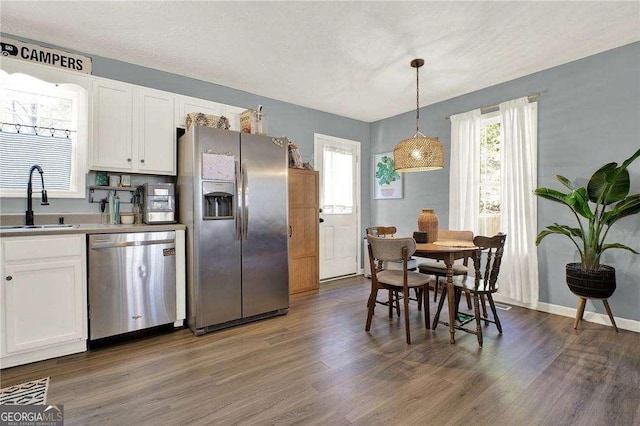 kitchen with pendant lighting, dark hardwood / wood-style floors, white cabinets, appliances with stainless steel finishes, and sink