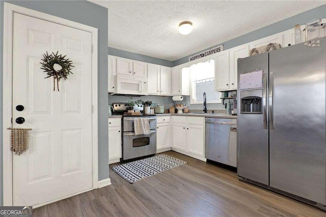 kitchen with sink, a textured ceiling, white cabinetry, hardwood / wood-style flooring, and appliances with stainless steel finishes